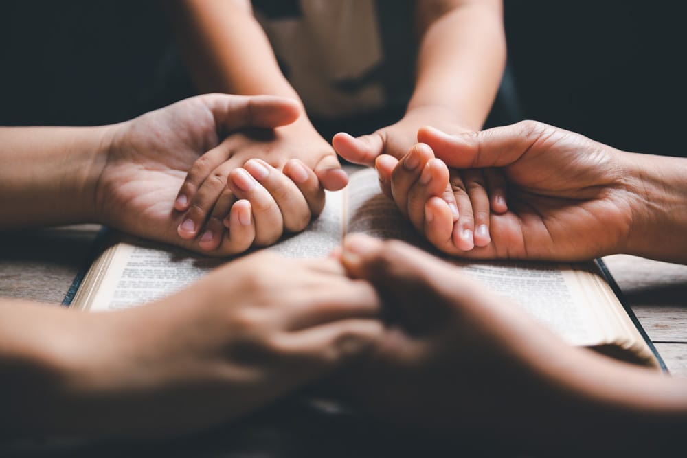 Familia tomandose de las manos encima de una biblia abierta
